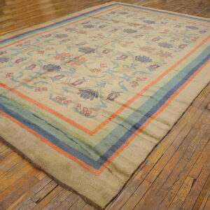Beige floral rug with coral, blue, and teal striped borders displayed on rustic wooden floorboards.