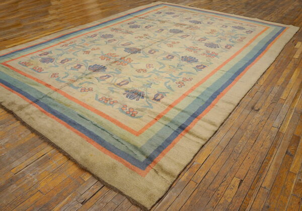 Beige floral rug with coral, blue, and teal striped borders displayed on rustic wooden floorboards.