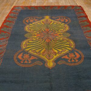 Dark blue rug featuring a vibrant yellow and orange stylized central design on distressed wood flooring.