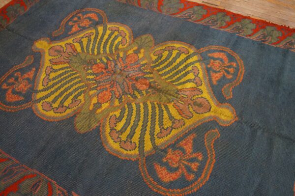 Blue rug with a yellow, striped, and orange medallion, bordered in red and green, resting on wood floor.