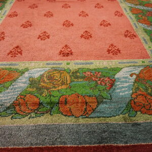 Close-up of a rug with a salmon pink field and pictorial borders of orange flowers, green leaves, and blue water.
