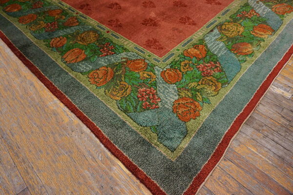 Close-up of a red rug border displaying stylized orange and green flowers on distressed wood flooring.