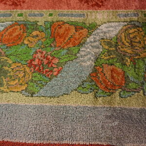 Close-up of a rug border showing a colorful floral motif with orange, green, yellow, and blue on a textured pile.