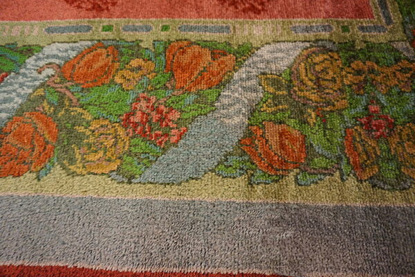 Close-up of a rug border showing a colorful floral motif with orange, green, yellow, and blue on a textured pile.
