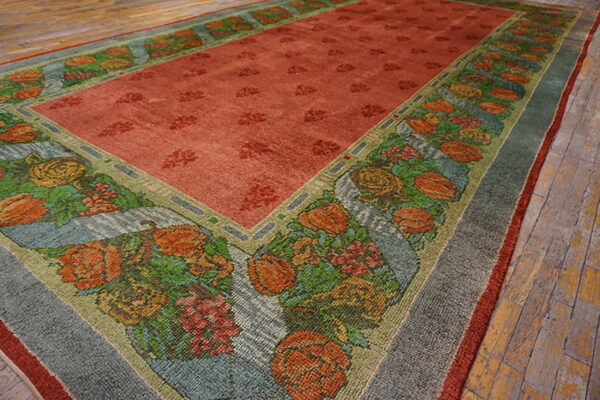 The rust rug field has a dense floral border featuring orange, green, blue, and yellow patterns over distressed wood flooring.