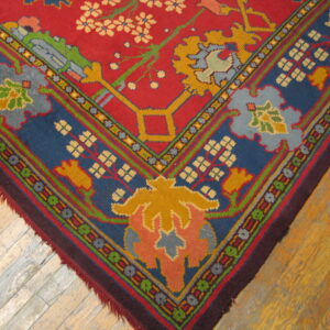 Vibrant red rug corner featuring complex blue, gold, and green floral patterns rests on wood planks.