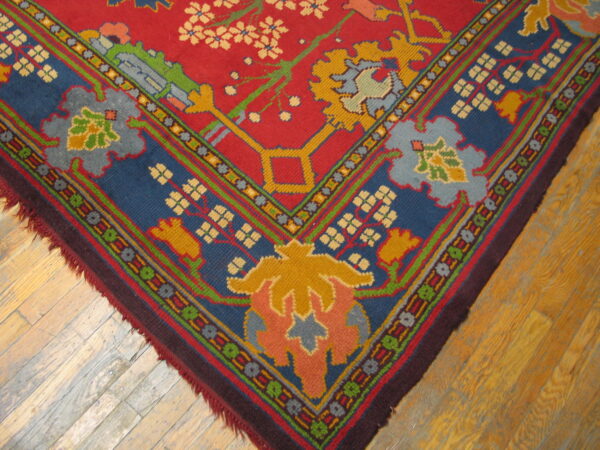Vibrant red rug corner featuring complex blue, gold, and green floral patterns rests on wood planks.