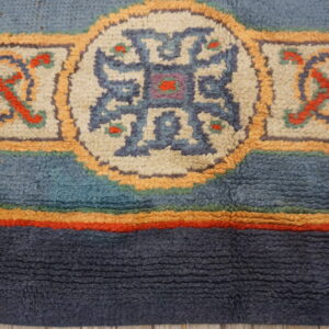 Textured rug detail with thick navy and blue bands bordering geometric medallions in cream and orange.