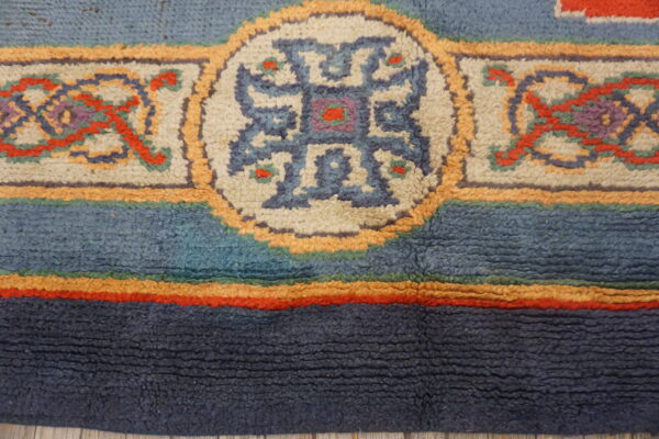 Textured rug detail with thick navy and blue bands bordering geometric medallions in cream and orange.