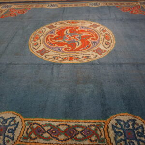 Close view of a slate blue rug with a circular orange medallion and complex multicolored borders.