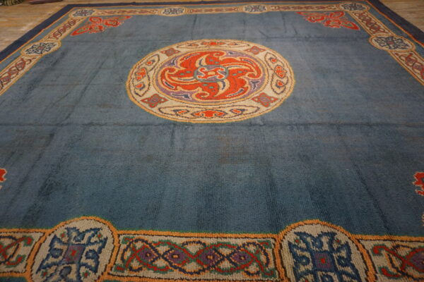 Close view of a slate blue rug with a circular orange medallion and complex multicolored borders.