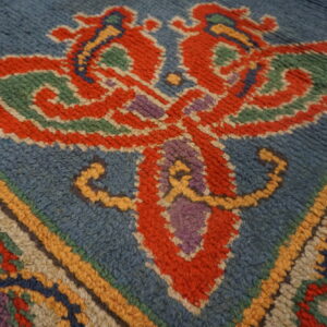 Close-up shows a red, green, and purple abstract motif against a fuzzy blue high-pile rug.