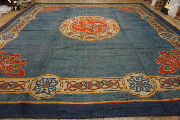 Slate blue rug with ornate red, cream, and purple medallion and complex multicolored borders on wood flooring.