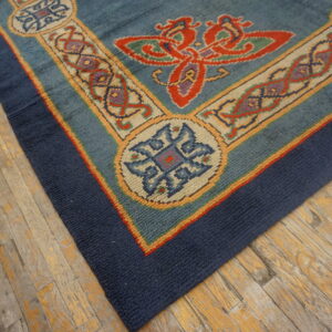 Textured blue rug with red and gold stylized borders lies diagonally on worn hardwood flooring.