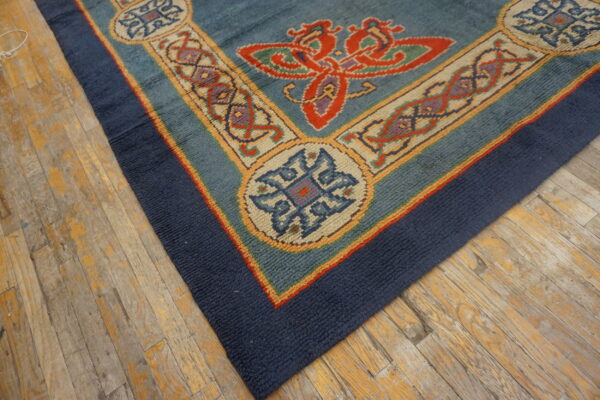 Textured blue rug with red and gold stylized borders lies diagonally on worn hardwood flooring.