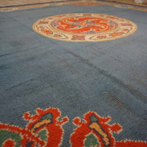 Textured blue area rug with a vibrant orange and cream central medallion on a light wood floor.