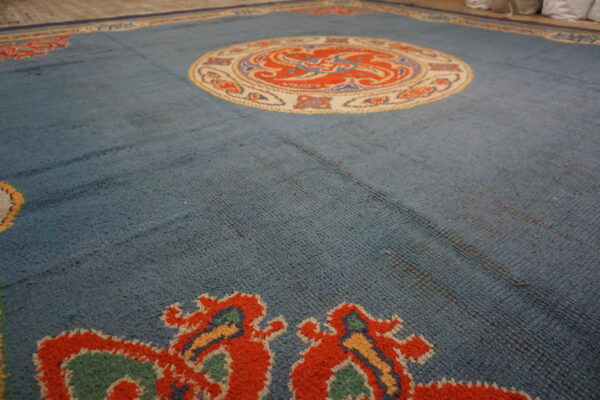 Textured blue area rug with a vibrant orange and cream central medallion on a light wood floor.