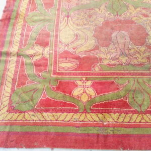 Ornate area rug in faded red, olive green, and yellow featuring complex floral designs and multiple borders on a pale floor.