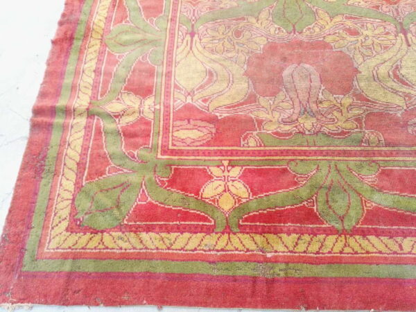 Ornate area rug in faded red, olive green, and yellow featuring complex floral designs and multiple borders on a pale floor.