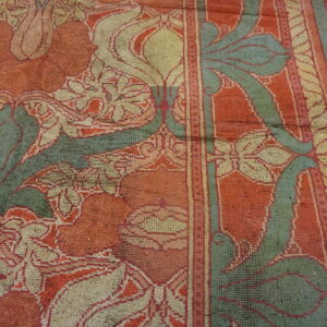 Muted orange, sage green, and cream floral rug showing wear and a distinct striped border detail.