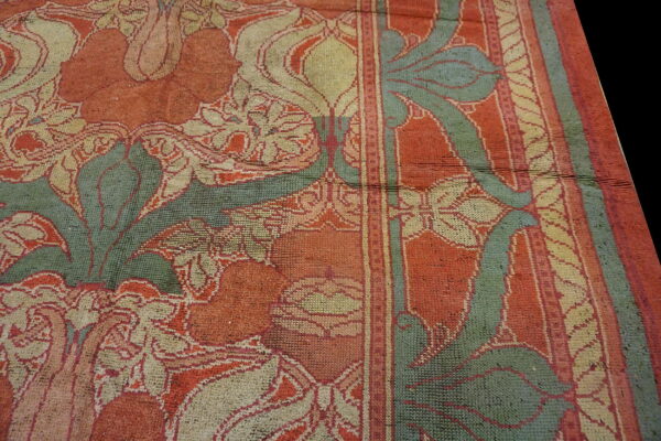 Muted orange, sage green, and cream floral rug showing wear and a distinct striped border detail.