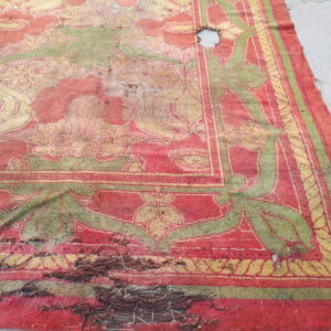 Distressed red and olive green floral rug on concrete with a large hole and noticeable thread unraveling.