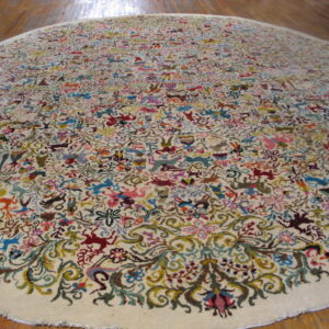 Round, low pile cream rug with a busy multicolored folk pattern of animals on a wood floor.