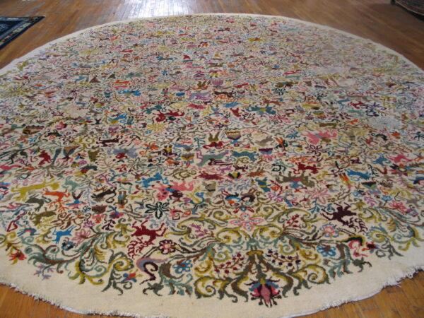 Round, low pile cream rug with a busy multicolored folk pattern of animals on a wood floor.