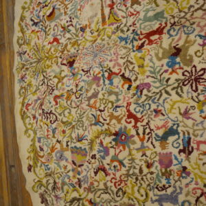 Multicolored folk figures and animals densely fill the high-pile, ivory field of this rug lying on wood planks.