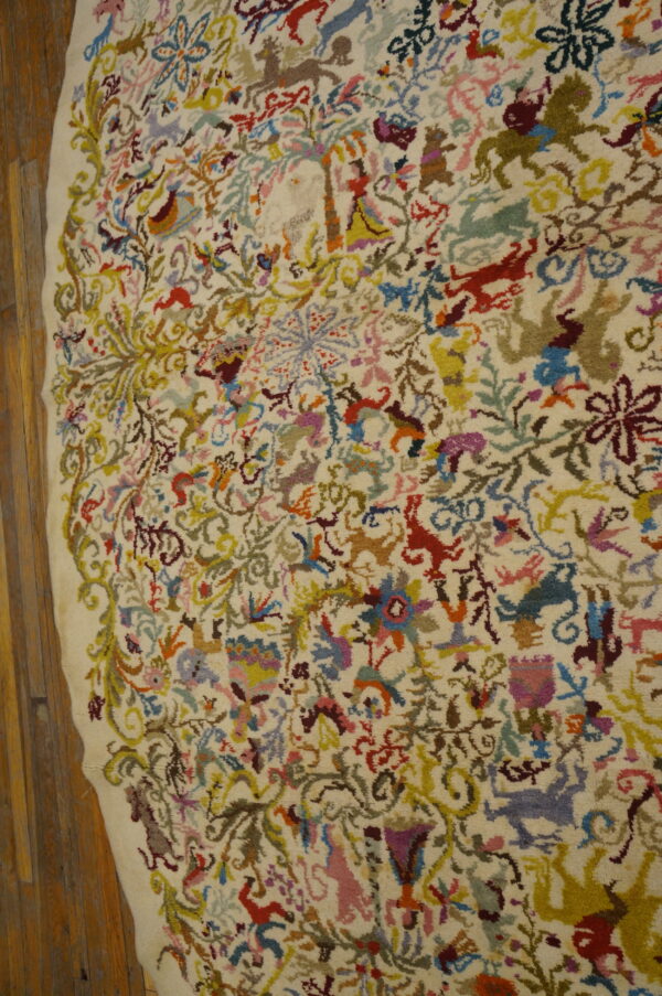 Multicolored folk figures and animals densely fill the high-pile, ivory field of this rug lying on wood planks.