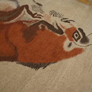 Textured beige rug featuring a painterly rust and brown abstract animal design near distressed wood flooring.
