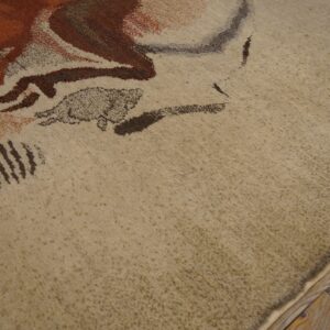 Close-up of a beige high-pile rug featuring abstract brown and rust colored patterns on rustic wood flooring.