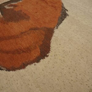 Detail view of a rug showing rusty orange shapes against a textured beige background.