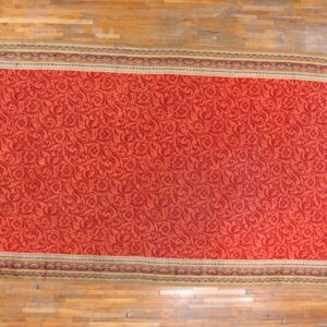 Large red rug with a tone-on-tone scroll pattern and multicolored border resting on wood plank floors.