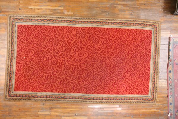 Large red rug with a tone-on-tone scroll pattern and multicolored border resting on wood plank floors.