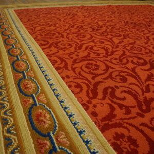 Terra cotta rug with damask field and colorful blue and gold border rests on hardwood floor.