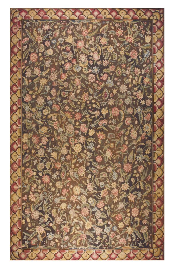 Low-pile rug with a dark field covered in dense floral motifs, framed by a red and tan scalloped border.