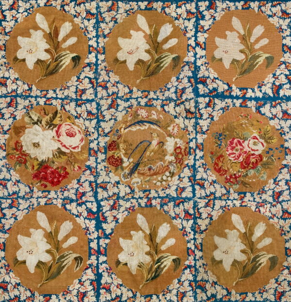 Detailed, low-pile rug with tan floral medallions, featuring lilies and roses, on a dense blue leafy field.