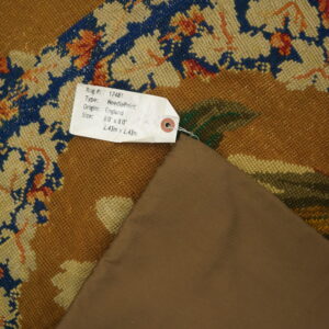 Low-pile rug with blue and rust floral patterns on a camel field, folded to show the brown backing material.