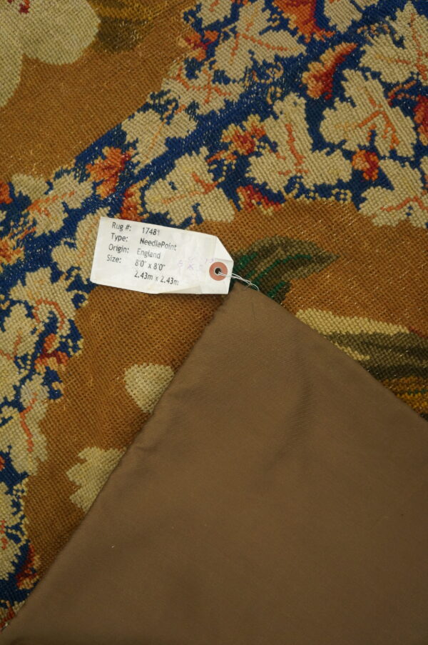 Low-pile rug with blue and rust floral patterns on a camel field, folded to show the brown backing material.