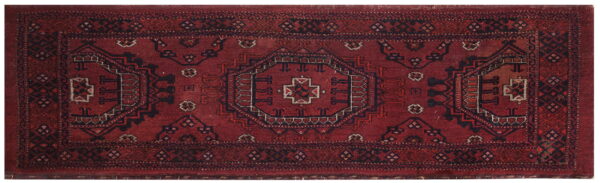 Red runner rug featuring traditional geometric patterns in dark blue, black, and tan accents.