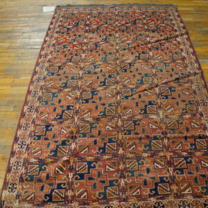 Low-pile rug with geometric patterns in rust, navy, and teal on distressed wood floors.