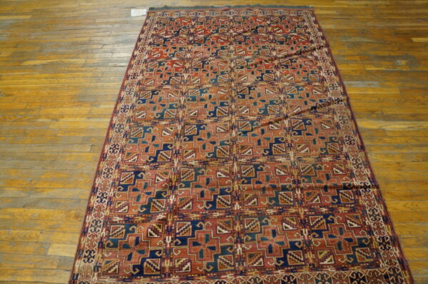 Low-pile rug with geometric patterns in rust, navy, and teal on distressed wood floors.