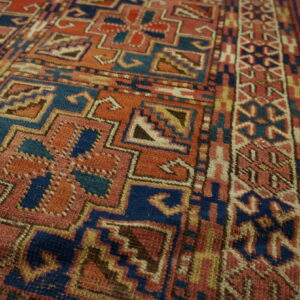 Textured geometric rug in rust, indigo, and cream colors lies on polished wood plank flooring.