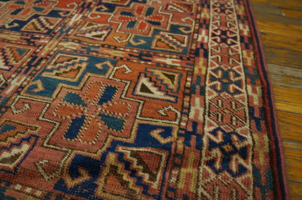 Textured geometric rug in rust, indigo, and cream colors lies on polished wood plank flooring.
