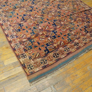 Rust and indigo geometric patterned rug with a low pile rests on worn yellow wooden planks.