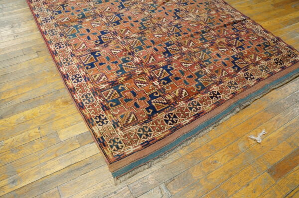 Rust and indigo geometric patterned rug with a low pile rests on worn yellow wooden planks.