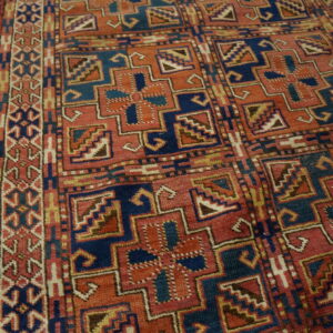 Geometric rug featuring stepped medallions in rust and indigo blue rests on light hardwood planks.