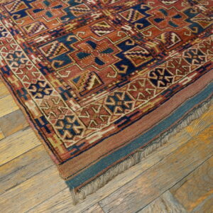 Terracotta and blue geometric patterned rug corner rests on rustic wide-plank wood flooring.