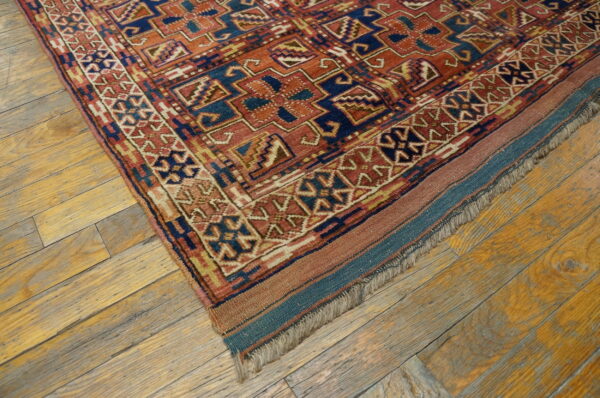 Terracotta and blue geometric patterned rug corner rests on rustic wide-plank wood flooring.
